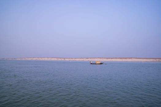 landscape view of Padma river on a fishing boat with a sand island under the blue sky