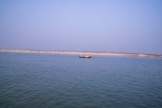 landscape view of Padma river on a fishing boat with a sand island under the blue sky