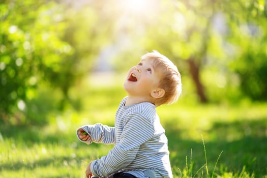 Cute laughing child sitting on the green spring meadow. Concept of the family and love.