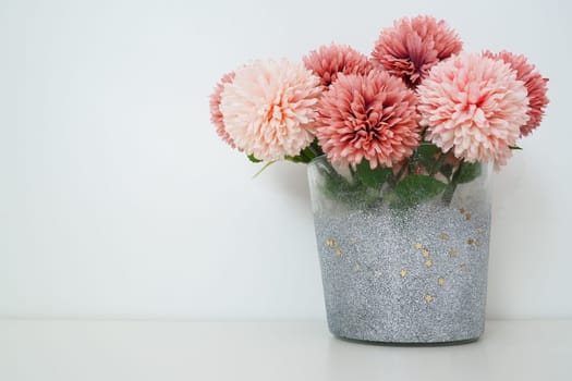 Bouquet of pink terry artificial flowers in a gray silver vase on a white background. Still life, interior decoration option. Room decor. Free space for text