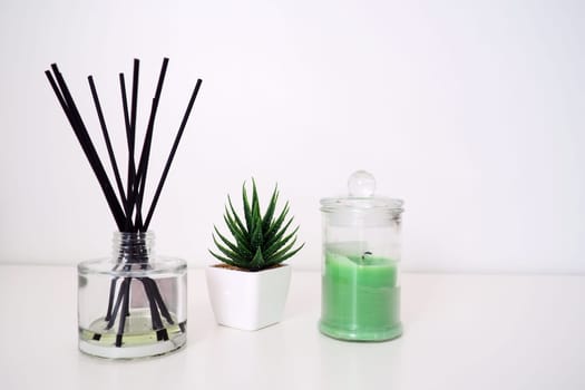 Incense sticks in a glass cubic vessel with essential oils. Interior decor. White background. Sansevier or aloe plant in a pot. Copy space. Wax candle in a stylish glass flask with a lid.