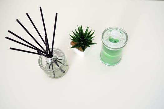 Incense sticks in a glass cubic vessel with essential oils. Interior decor. White background. Sansevier or aloe plant in a pot. Copy space. Wax candle in a stylish glass flask with a lid.