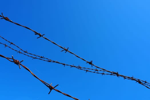 Barbed wire, wire, narrow strip of metal tape, with sharp spikes located on it, used to make barriers. Rusty barbed wire against the blue sky. The concept of war, restrictions on rights and freedoms