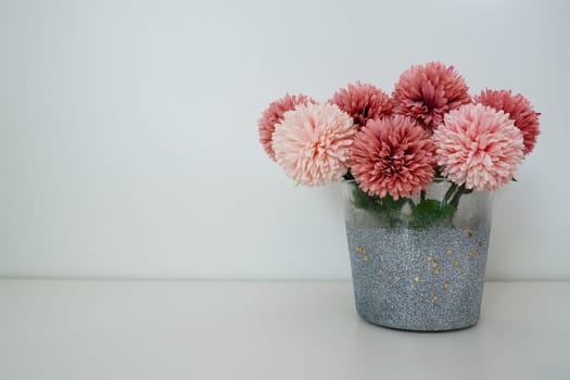 Bouquet of pink terry artificial flowers in a gray silver vase on a white background. Still life, interior decoration option. Room decor. Free space for text