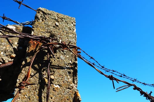Barbed wire, double wire, metal tape with sharp spikes for barriers. Rusty barbed wire against the blue sky. The concept of war, restriction of rights and freedoms. Concrete pillar