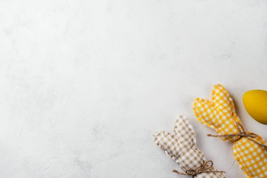 Easter postcard for celebration holiday, two handmade square brown, white and yellow colored bunnies with strings-scarfs on white gray paper background, yellow chicken egg. Copy space, place for text.