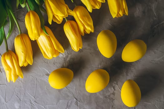 Easter eggs and bouquet of bright yellow tulips on gray concrete surface. Flat lay, top view