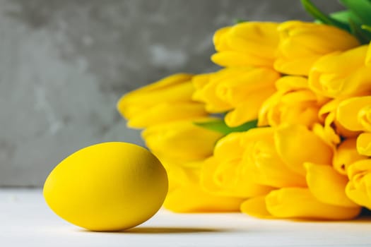 Bouquet of bright yellow tulips and Easter eggs lying on white wooden surface on gray background, copy space