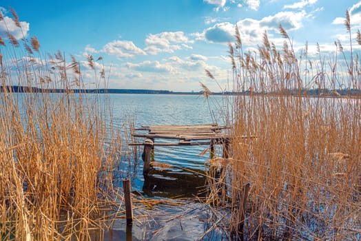 Fisherman's bridge and yellow brushwood and reeds near the blue water of the lake, Guyva river in Andrushivka, Ukraine