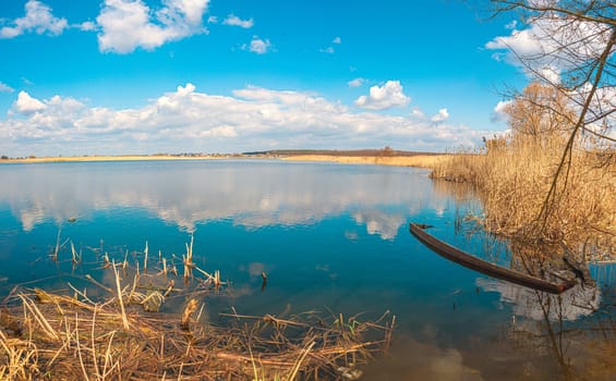 Flooded old wooden boat in blue water, yellow brushwood, and reeds, Guiva river in Andrushivka, Ukraine