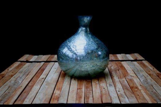 A still life with a blue vase on a stack of wooden slats, against a dark background.