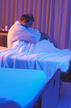 A depressed patient sits in a hospital bed.