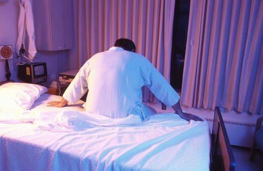 A ill patient sits anxiously on the edge of his hospital bed.
