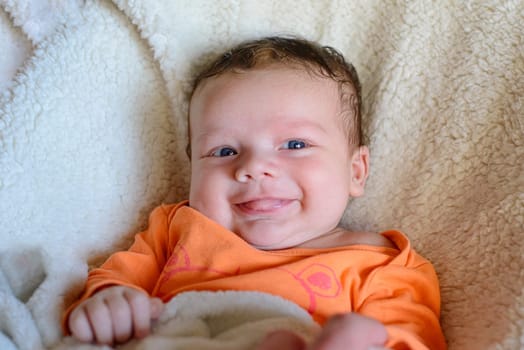 Smiling cute newborn white baby in orange clothes on a white blanket