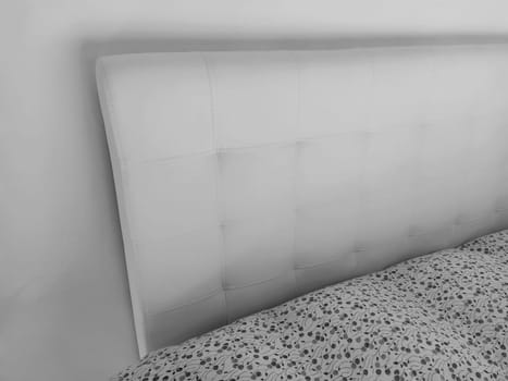 Soft headboard. Upholstery for furniture made of genuine or artificial leather and quilted fabric. Soft headboard against a light wall. Black and white monochrome photo.
