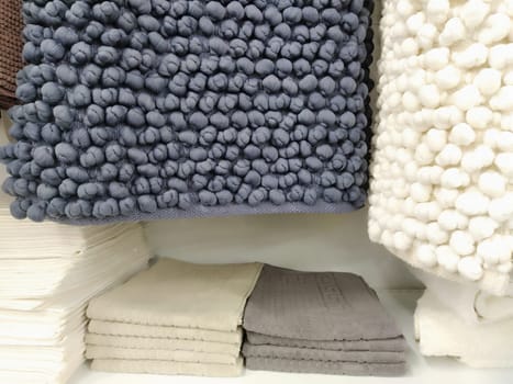 White and gray microfiber bath mats hang on a store counter. Scandinavian interior style. Soft pimply textile rectangular rugs with knitted pimples. Decoration and modern design of the bathroom.