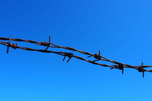 Barbed wire, wire, narrow strip of metal tape, with sharp spikes located on it, used to make barriers. Rusty barbed wire against the blue sky. The concept of war, restrictions on rights and freedoms
