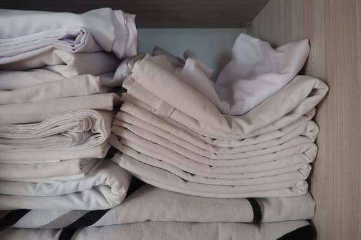 The white linens are stacked in the closet. Internal contents of a linen closet. Household organization. Hygienic conditions for sleep. Fabrics and bed sheets in half open white closet or wardrobe.