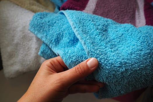 A woman's hand is feeling a cotton colored towel from a basket with dirty laundry. Laundry sorting and washing. Laundry room or bathroom. Housekeeping. Pink and blue terry towels