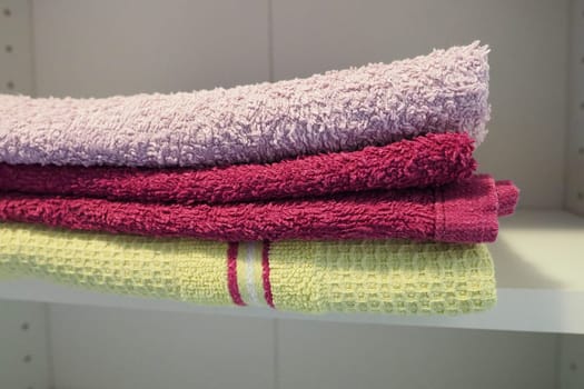 Towels on a shelf in a white cabinet. Clean ironed pink and yellow towels folded in a pile. Organization of household items in the bathroom or closet. The result of the work of a housewife