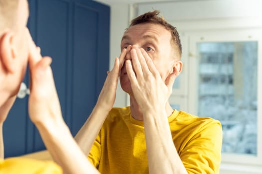 Mature man apply cosmetic product on face, then massage with hands. Male portrait in mirror massaging face. Skincare morning routine, careful beauty treatment, home lifestyle. Facial care concept.