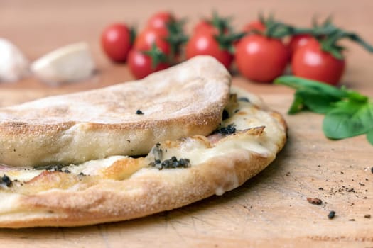 Italian food, closed calzone pizza on rustic wooden background. On blurred background small red tomatoes..Selective focus
