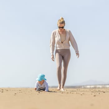 Mother playing his infant baby boy son on sandy beach enjoying summer vacationson on Lanzarote island, Spain. Family travel and vacations concept.