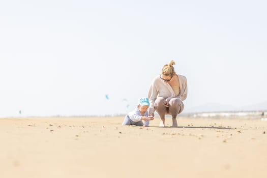 Mother playing his infant baby boy son on sandy beach enjoying summer vacationson on Lanzarote island, Spain. Family travel and vacations concept