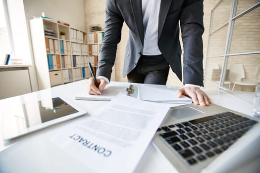 Male employee in suit making notes at workplace