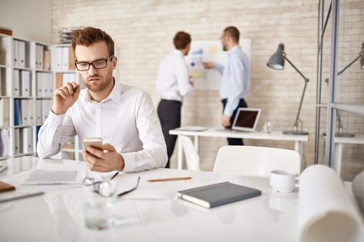 Serious businessman writing or reading sms in working environment