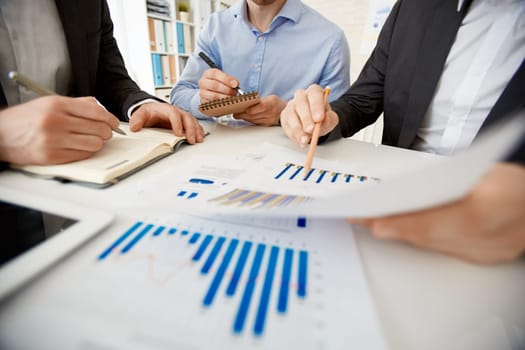 Businessman pointing at paper with chart while explaining it to colleagues at workplace