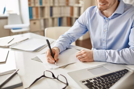 Smiling businessman writing down his ideas on paper at workplace
