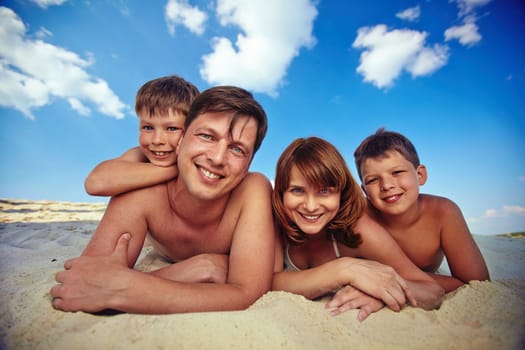 Young couple and two siblings lying on sand under cloudy sky