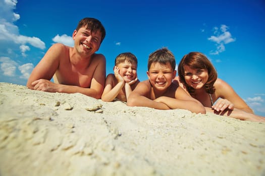 Happy family lying on sandy beach and looking at camera