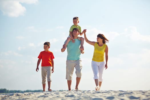 Happy family in casualwear walking on sandy beach