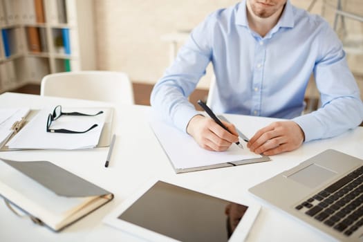 Serious businessman sitting at workplace with pen over paper