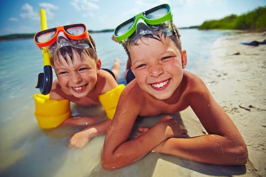 Happy siblings in goggles looking at camera on the beach