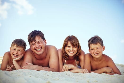 Happy family looking at camera while relaxing on sandy beach