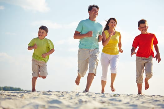 Modern family of four running on sandy beach