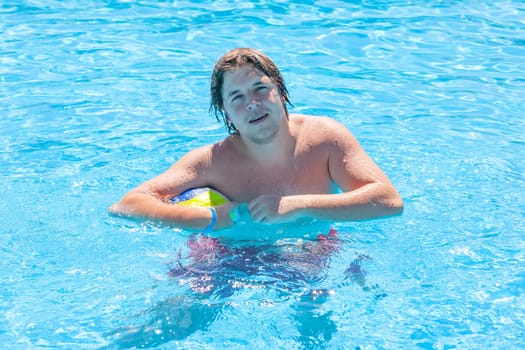 Happy man with water ball playing in a swimming pool in summer