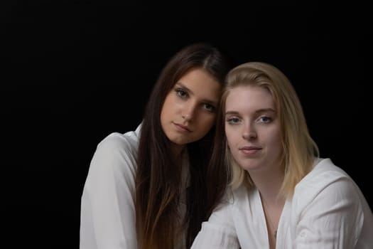 Low key portrait of beautiful two girls posing for the camera on the black background.  Horizontally.