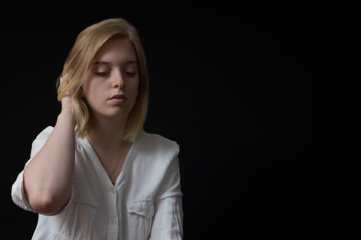 Low key portrait of blondes sad young woman weared in white shirt.