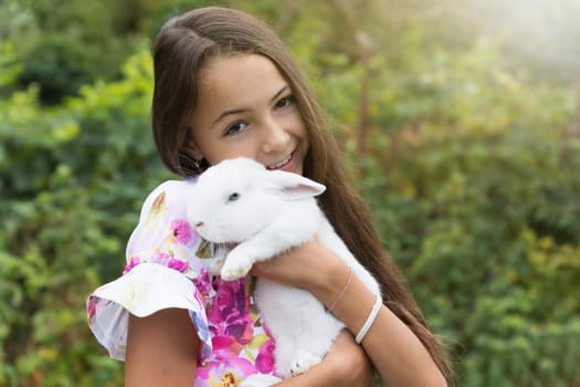 Little girl is holding a white rabbit in her arms outdoors. Easter concept.