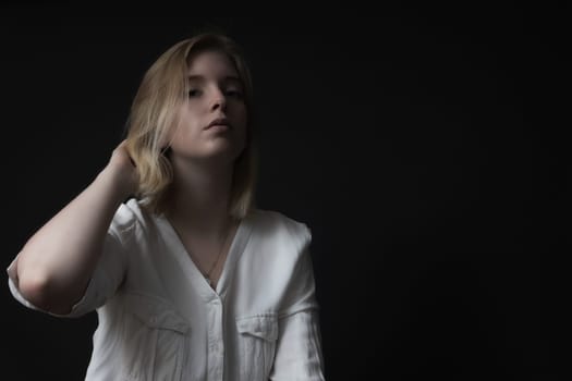 Serious blondes girl weared in white shirt is posing on black background.