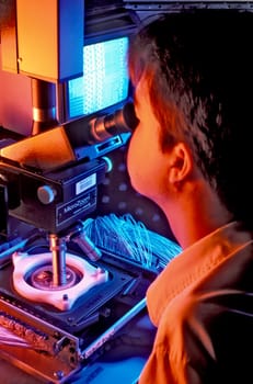 A man looking into a microscope in the semi- conductor industry.
