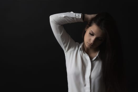 Low key portrait of long haired sad young woman weared in white shirt. Horizontally.