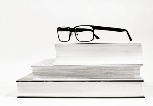 Three thick books and glasses as a visual aid as black and white picture