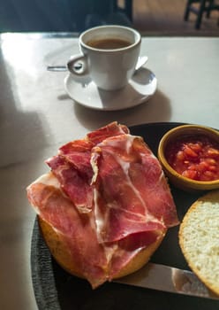 Cured ham toast with grinded tomato for breakfast. Coffee cup at bottom