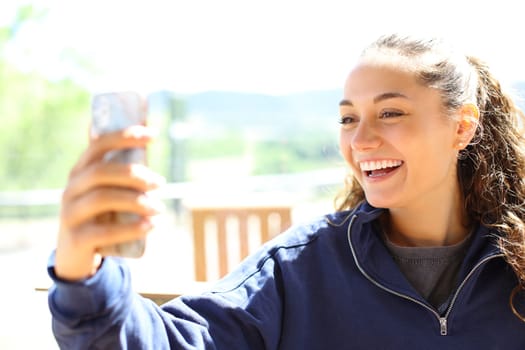 Happy woman in a terrace using phone laughing