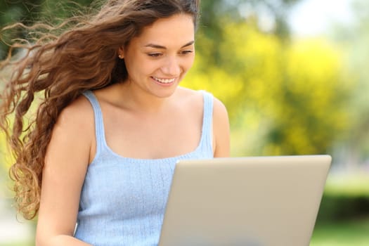 Happy woman using laptop sitting on a bench